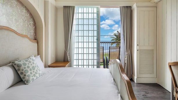 A hotel room with a large bed, a nightstand, a view of the outdoors, and a door leading to another room. - Southern France (Checheng)