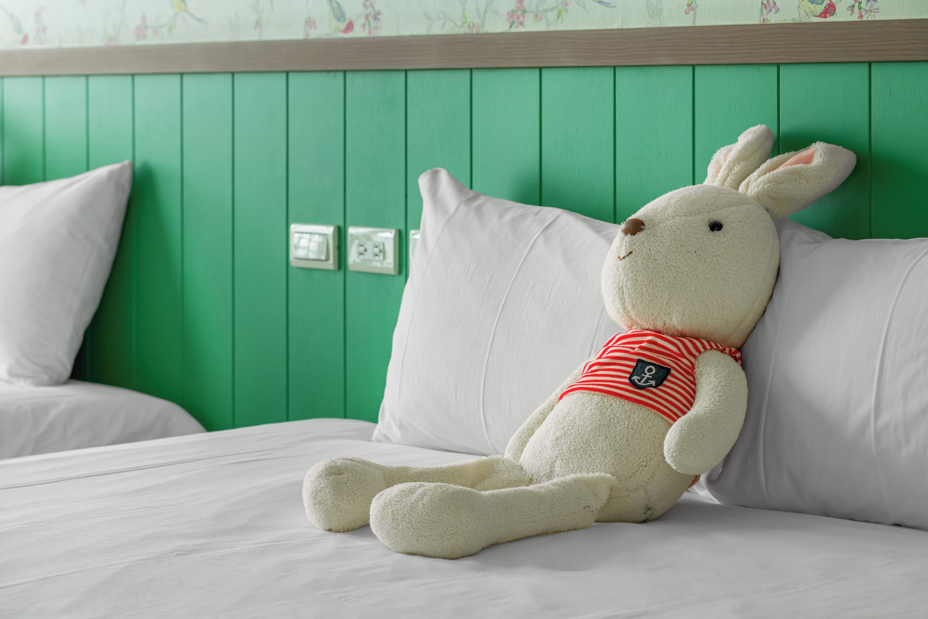Un conejo de peluche sobre una cama con ropa de cama blanca y paredes verdes.