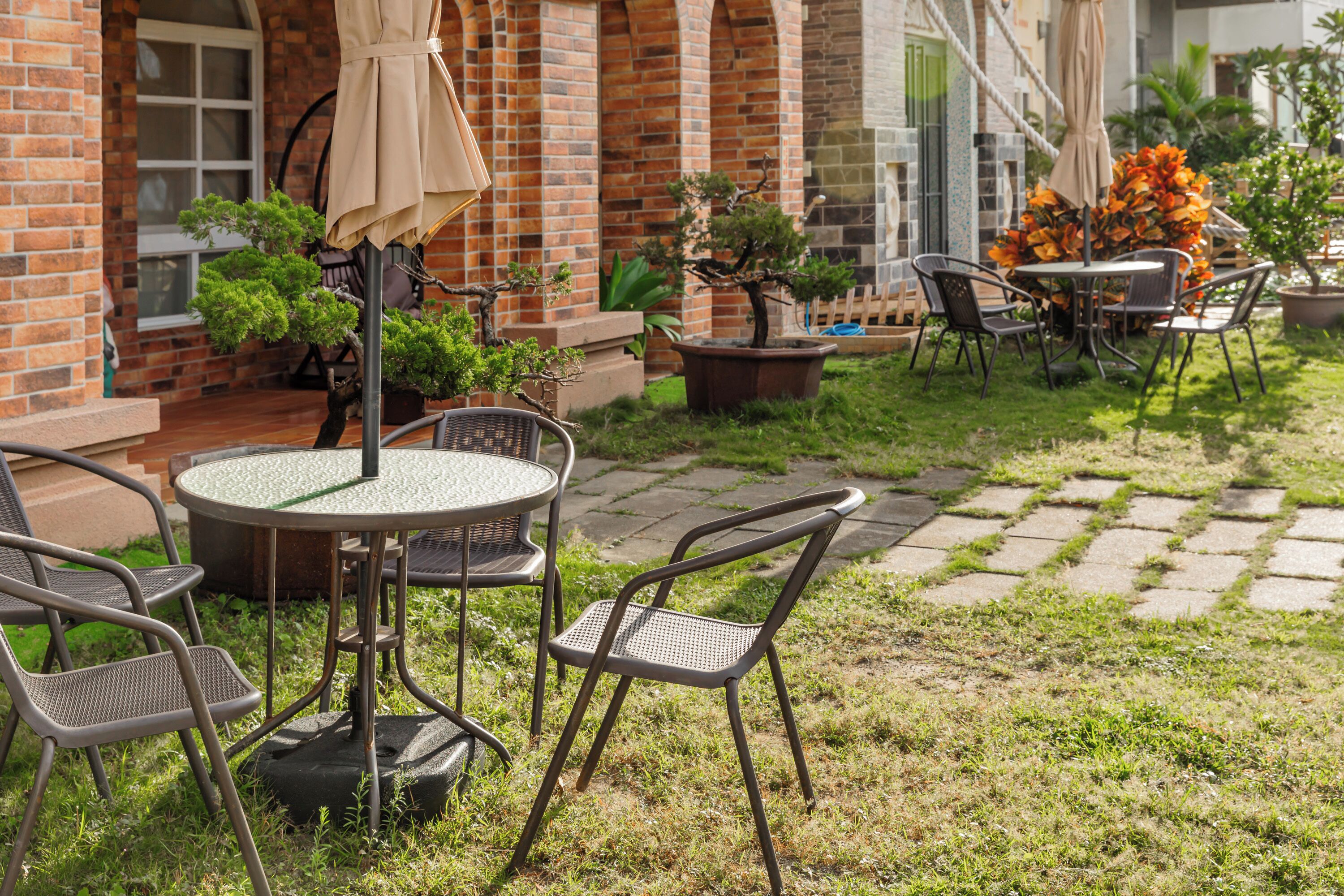 Une terrasse extérieure avec une table ronde et des chaises, entourée de plantes en pot et d’un mur de briques.