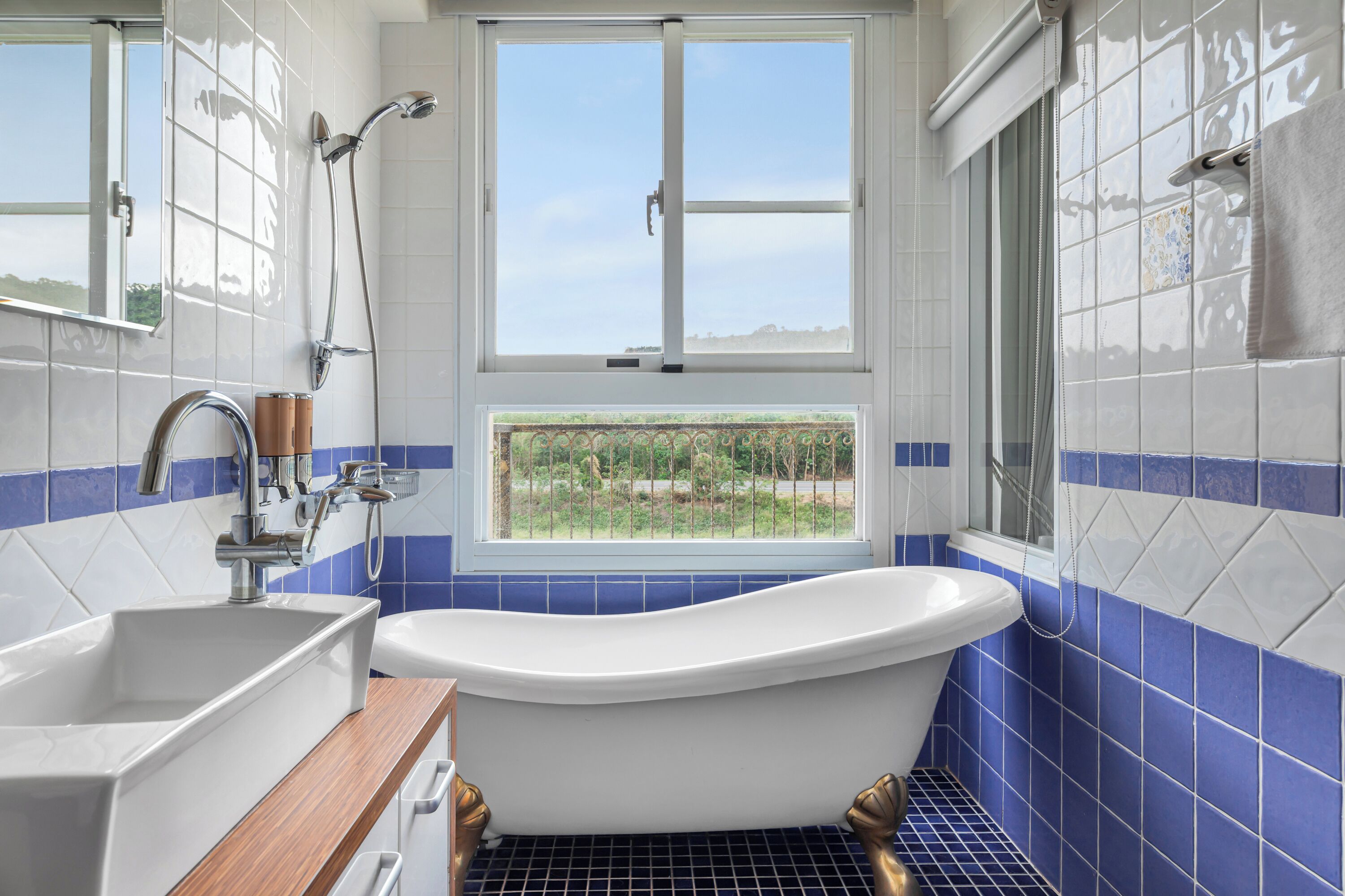 A bathroom with a bathtub, a sink, and a window with a view of greenery.