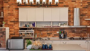 A kitchen with white cabinets, a brick wall, a countertop with various appliances, and a hanging light fixture. - Southern France (Checheng)