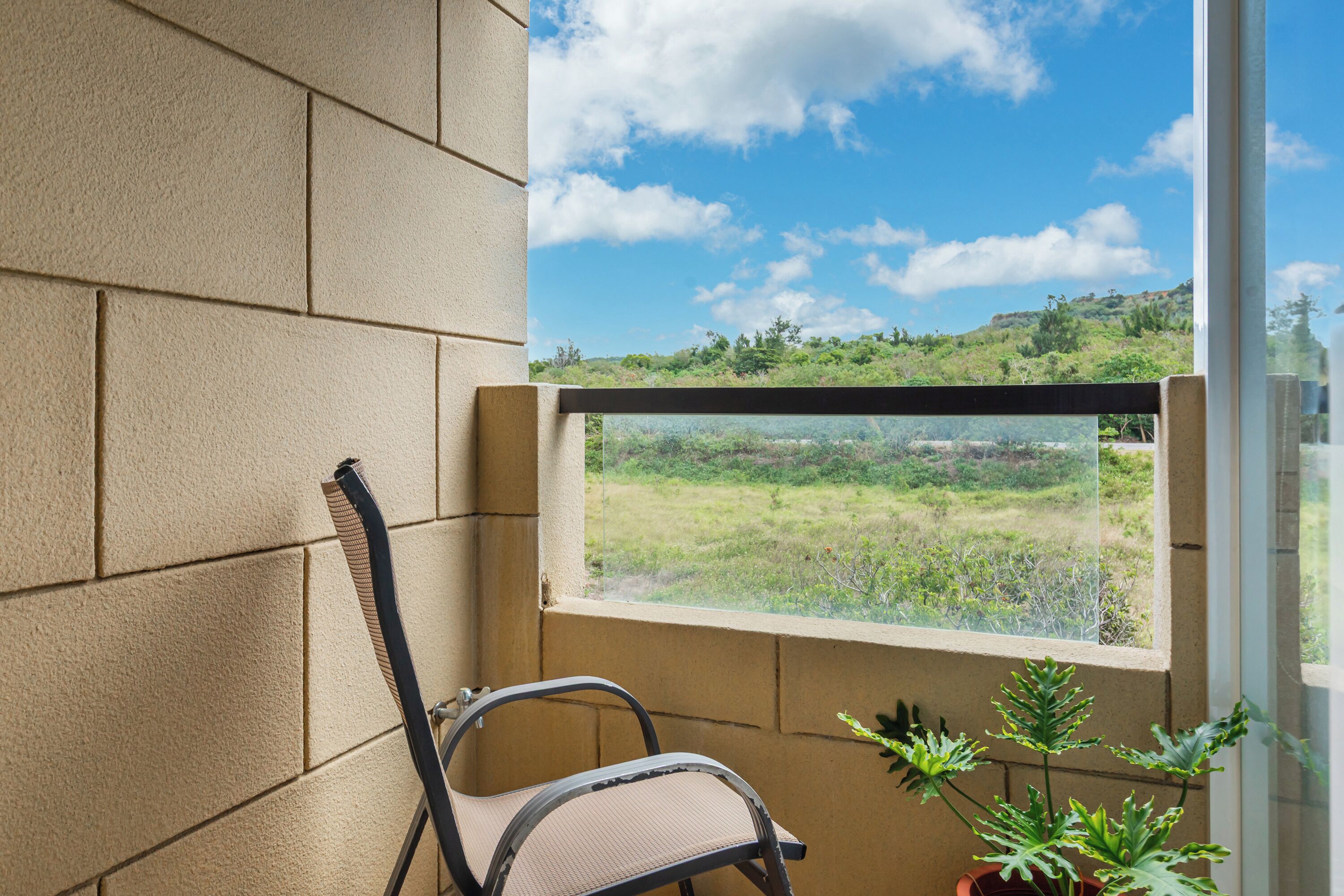 A balcony with a view of a green landscape, a chair, and potted plants.