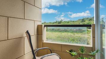 A balcony with a view of a green landscape, a chair, and potted plants.
