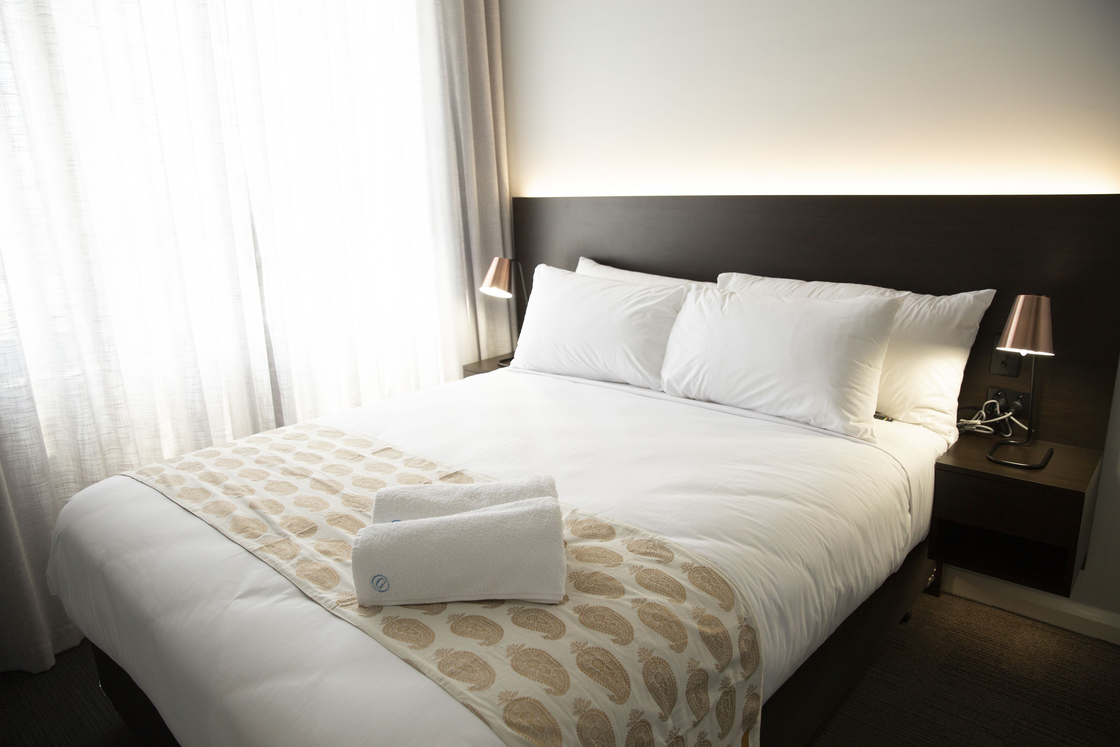 A neatly made bed with a patterned bedspread, two bedside lamps, and a nightstand with a phone.