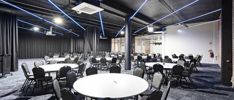 A conference room with multiple tables and chairs, ceiling lights, and a visible fire extinguisher.