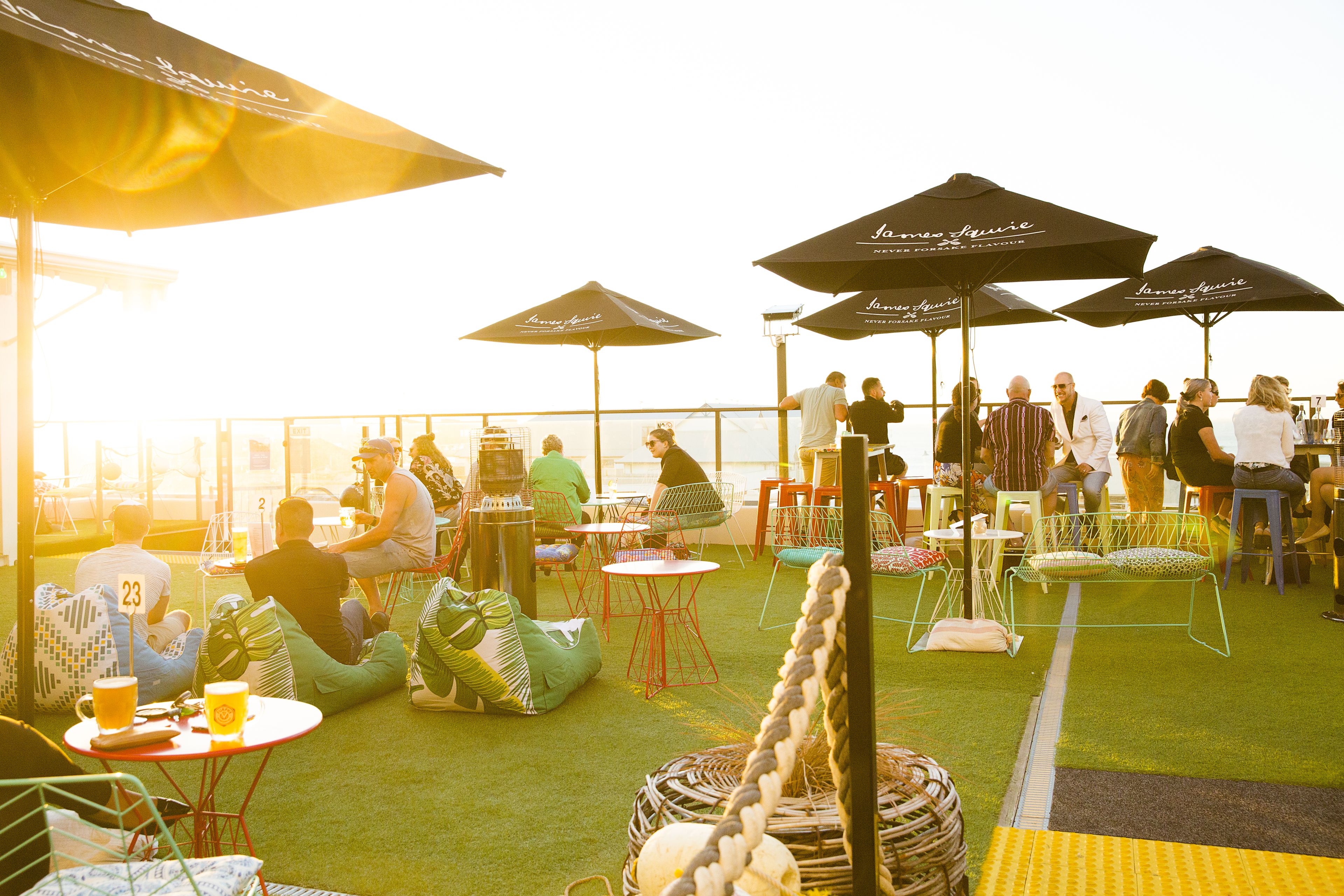 An outdoor seating area with tables and chairs, umbrellas, and a view of the sea.