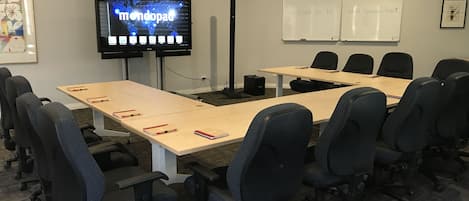 A conference room with a large screen displaying a world map, a whiteboard with a welcome message, and multiple tables and chairs.