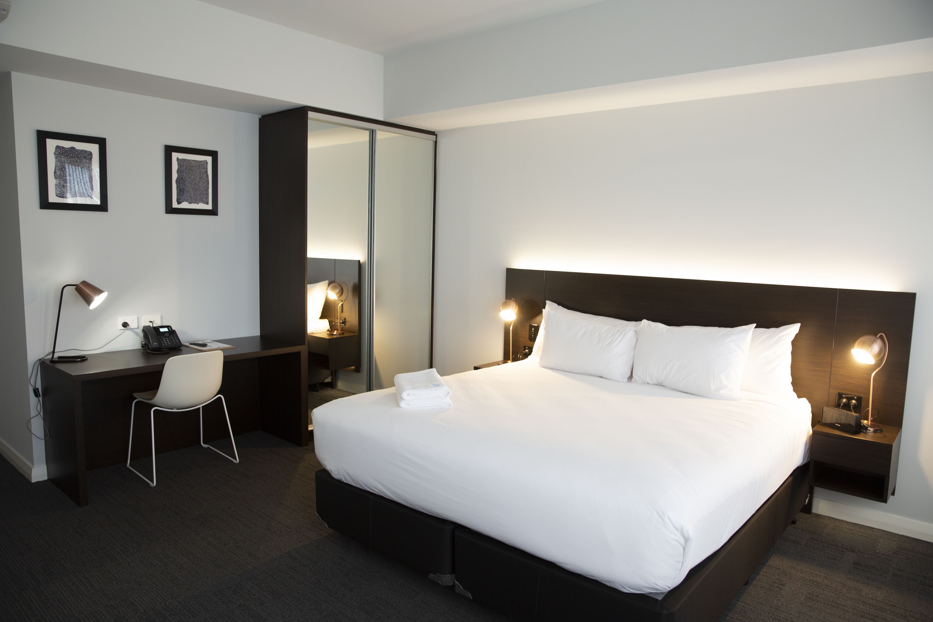 A hotel room with a large bed, a desk with a chair, a mirror, and two bedside lamps.
