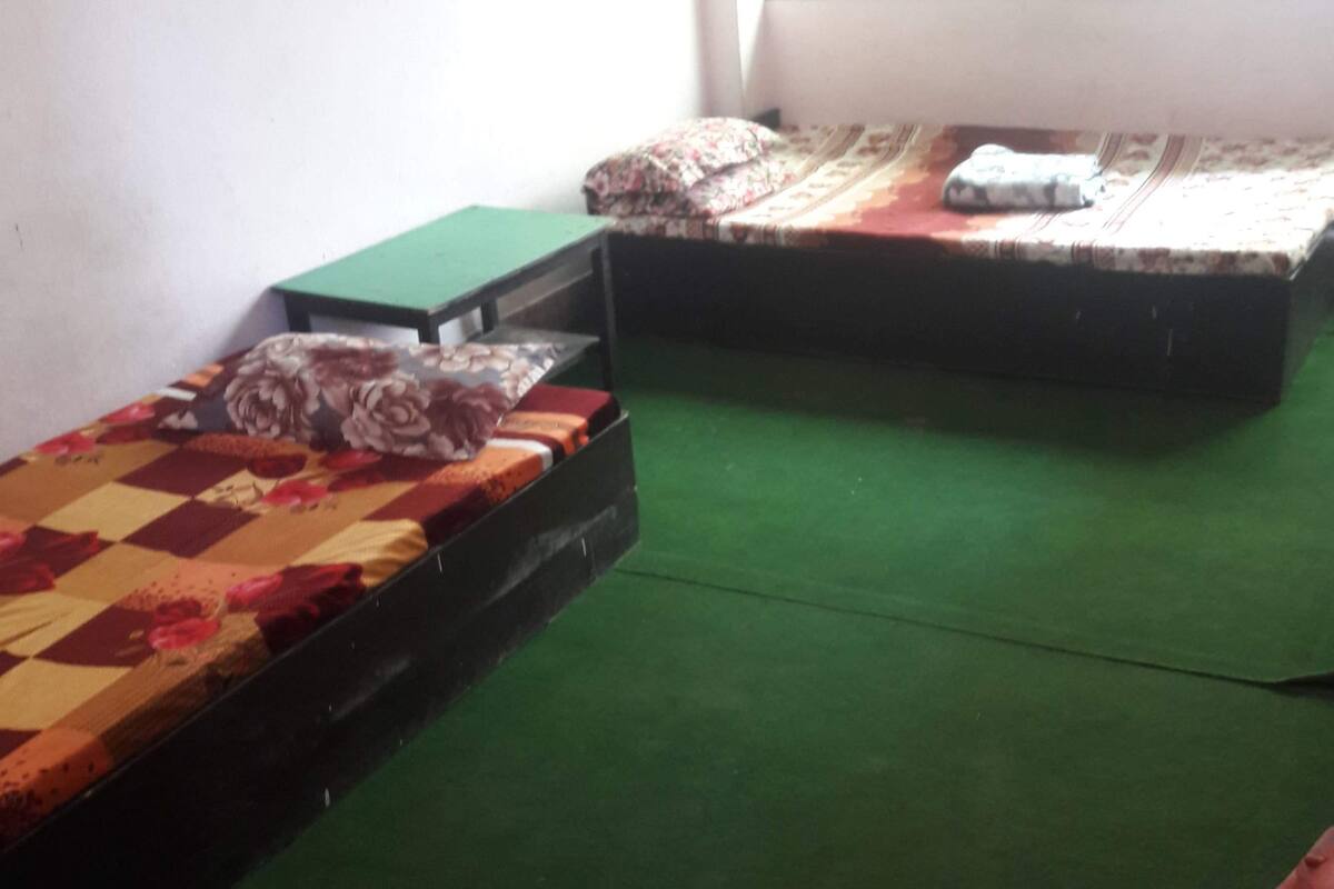 Two single beds with floral bedding, a green mat on the floor, and a small table with a green top.