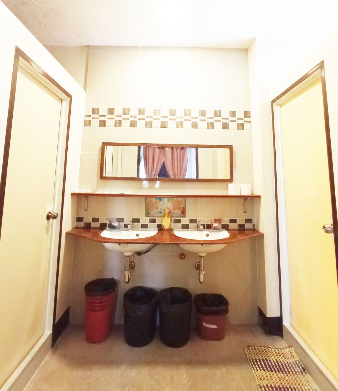 Une salle de bain avec deux lavabos, un miroir et trois poubelles.