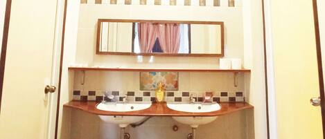 A bathroom with two sinks, a mirror, and three trash bins.