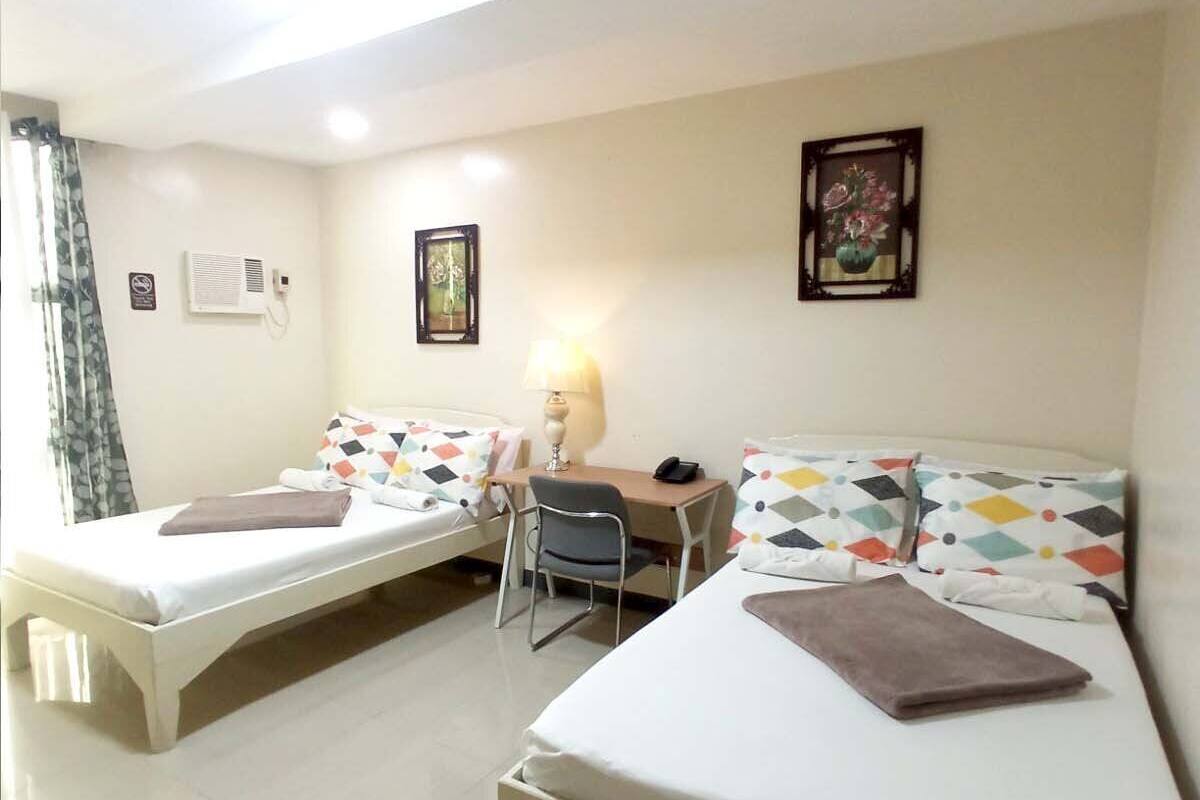 A hotel room with two single beds, a desk, a chair, a lamp, and a picture on the wall.