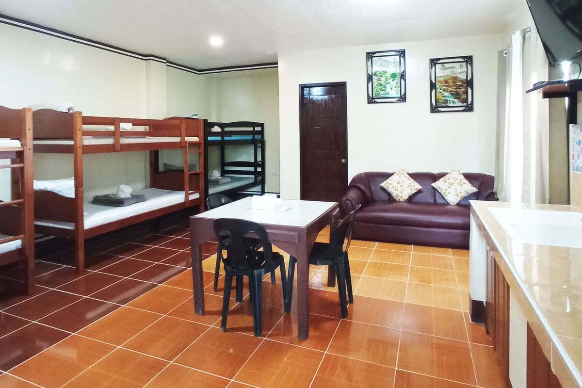 A room with bunk beds, a dining table with chairs, a sofa, and a television.