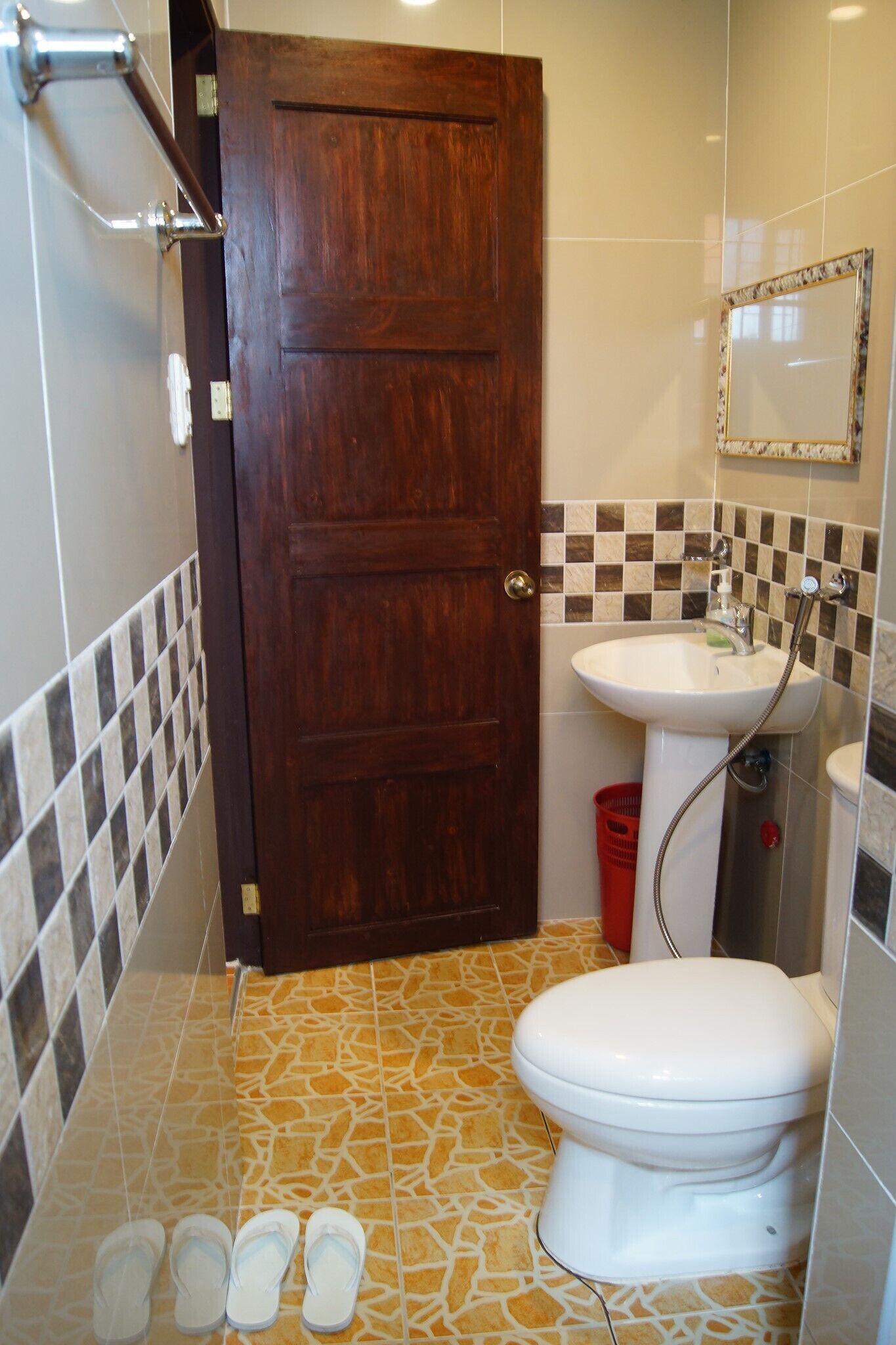 Un baño con puerta de madera, un lavabo blanco, inodoro y espejo.
