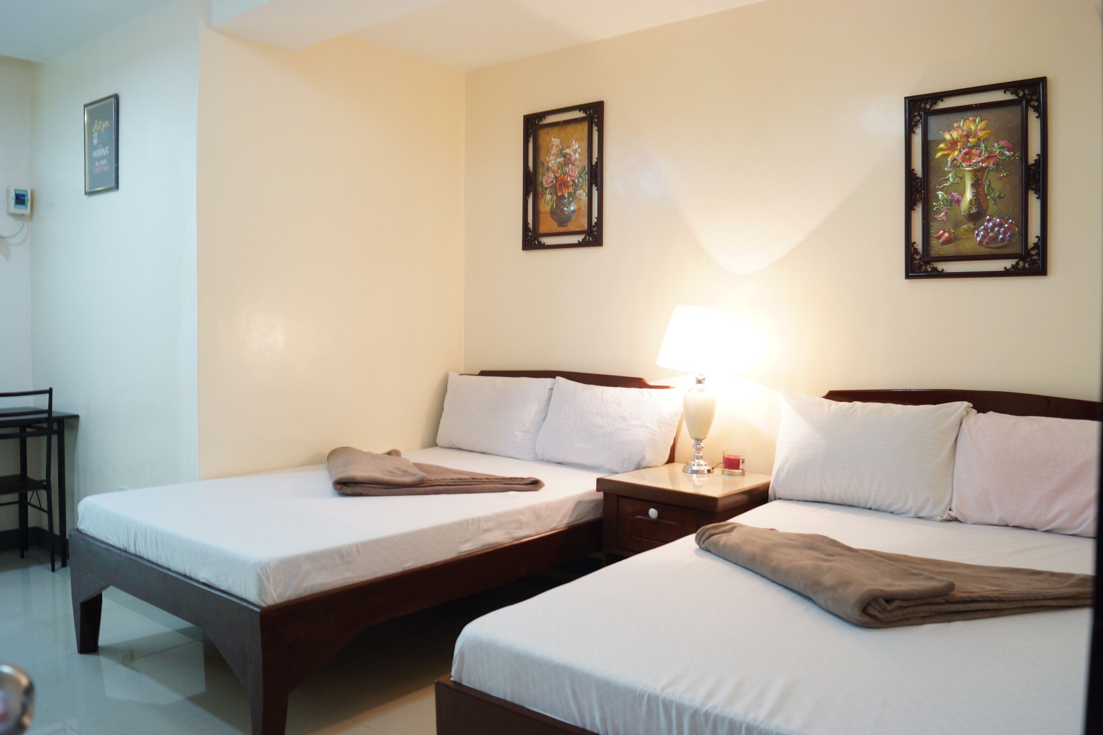 A hotel room with two beds, a nightstand with a lamp, and two framed pictures on the wall.