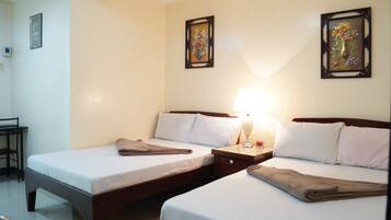 A hotel room with two beds, a nightstand with a lamp, and two framed pictures on the wall.