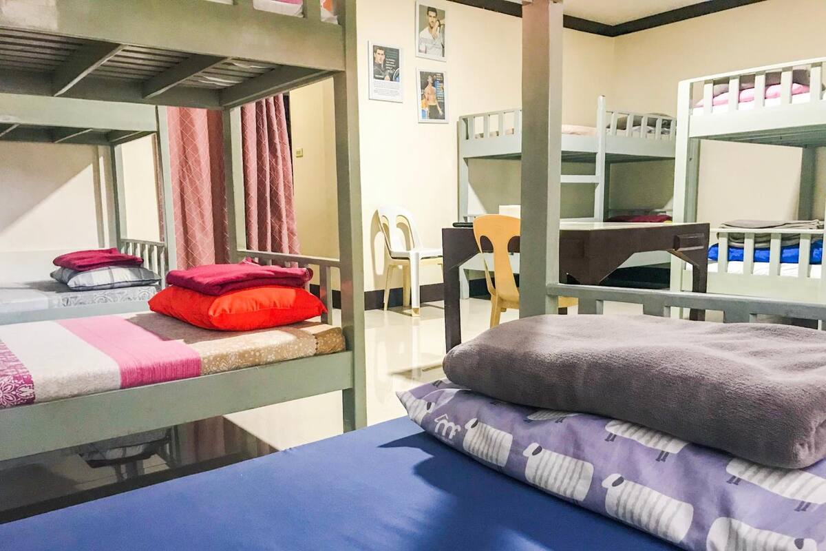 A dormitory room with bunk beds, a desk, and chairs.