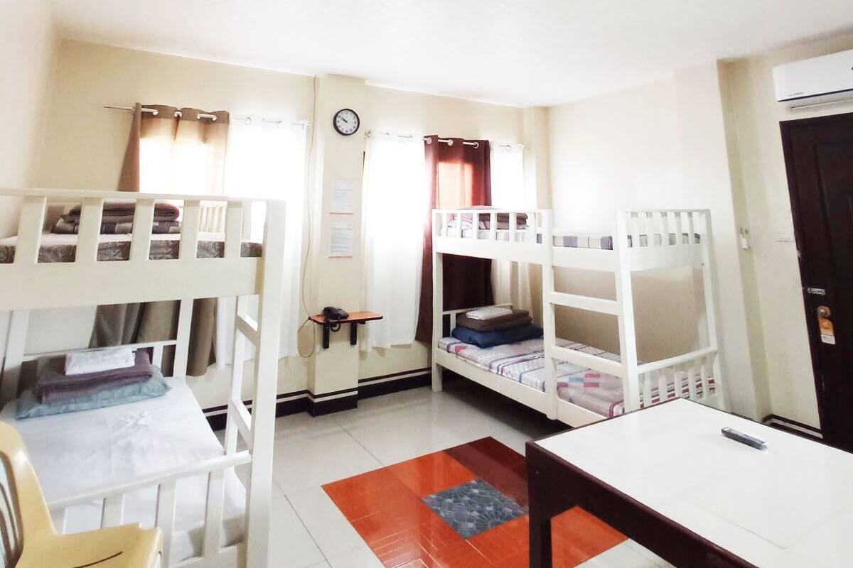 A room with bunk beds, a desk, a chair, a clock, and an air conditioning unit.