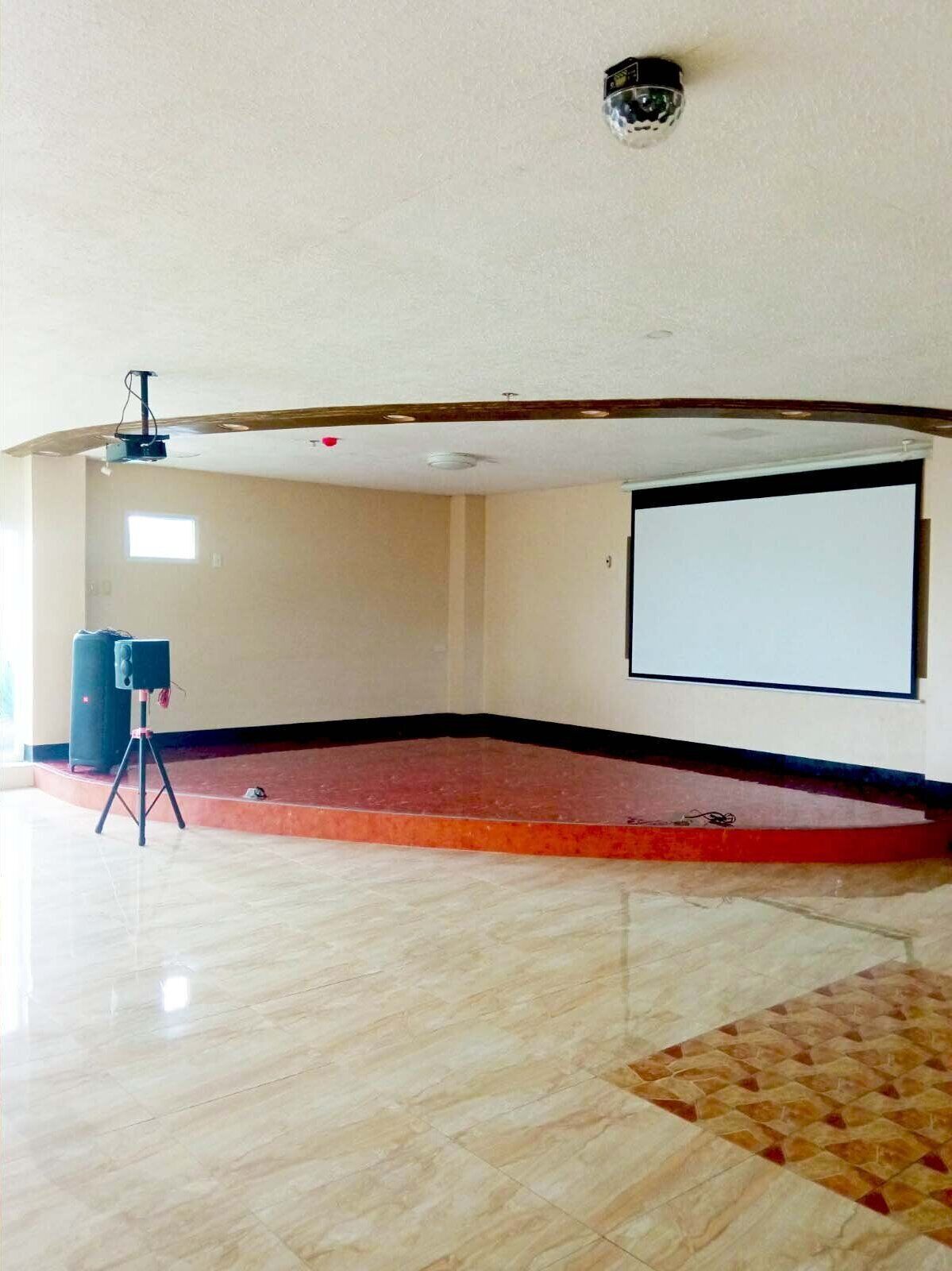 Une salle équipée d’un grand écran, d’un projecteur et d’un haut-parleur posé sur un support.