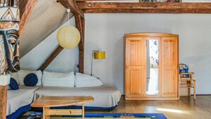 A room with a loft bed, a wooden wardrobe, a small table, and a floor lamp.
