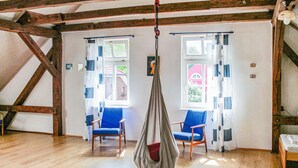 A room with wooden beams, two blue chairs, a hanging chair, and a window with a view of a building.
