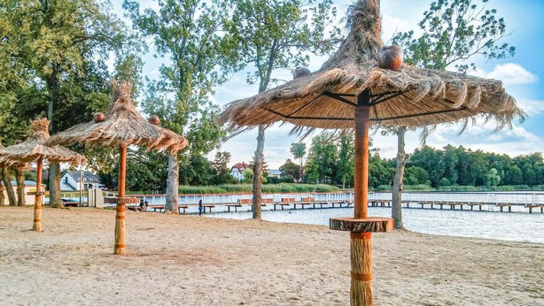 A beach with thatched umbrellas and a wooden pier extending into the water.