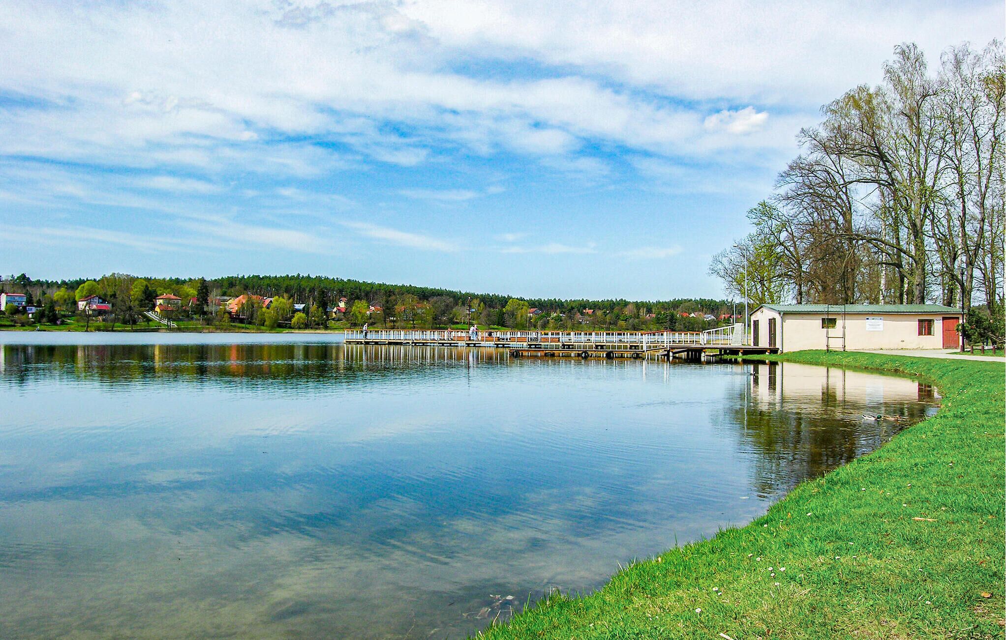 Un lac paisible avec une jetée qui s’avance sur l’eau, entouré de verdure et d’un petit bâtiment.