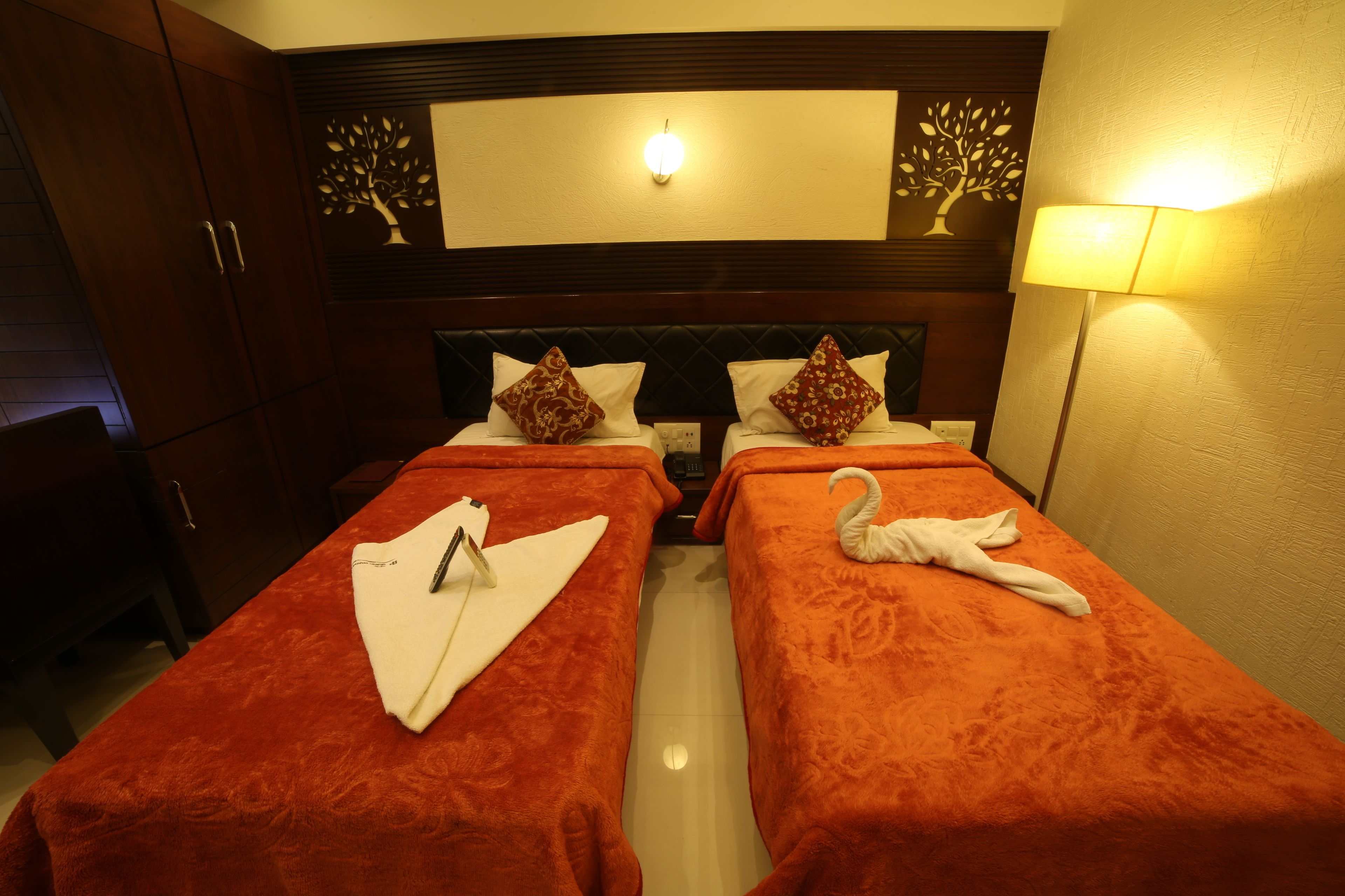 Quarto de hotel com duas camas, cada uma com colcha e almofadas vermelhas, cabeceira de madeira e luminária fixada na parede.
