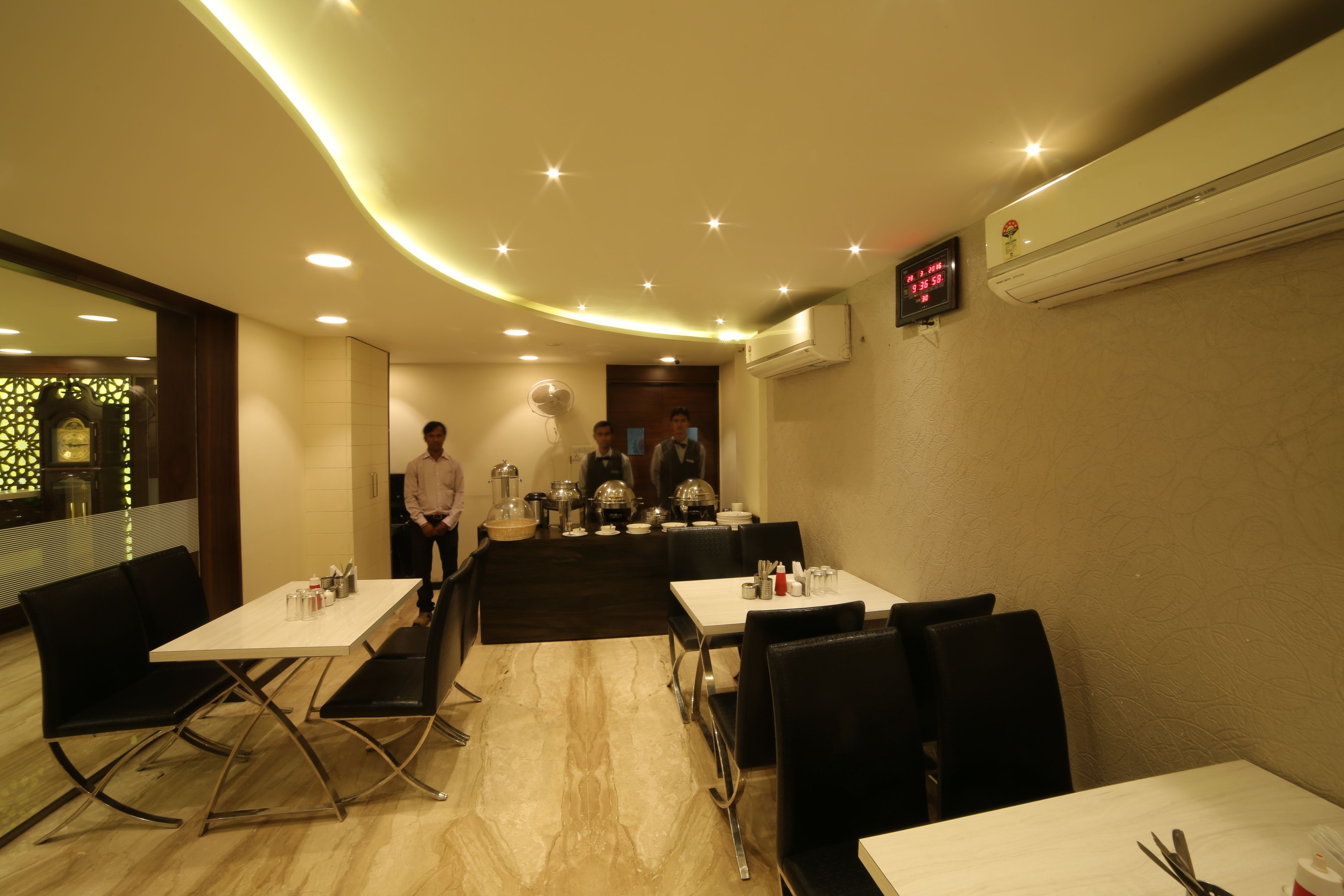 Un restaurante con mesas y sillas, una zona de cocina y un equipo de aire acondicionado en la pared.