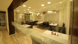 A modern restaurant with glass partitions, tables, and chairs. - Hotel Grandpragati (Surat)