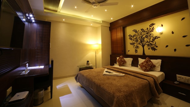 A hotel room with a bed, a desk, a chair, a lamp, and a wall decoration. - Hotel Grandpragati (Surat)