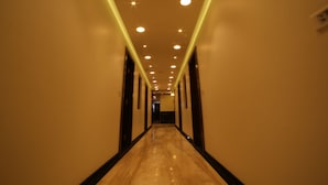A long, narrow hotel corridor with a polished floor, recessed lighting, and dark-framed doors. - Hotel Grandpragati (Surat)