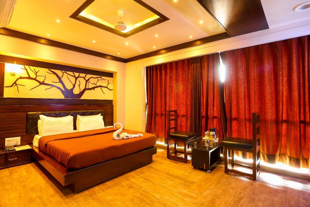 A hotel room with a large bed, a desk with a chair, a coffee maker, and a view of the outside through red curtains.
