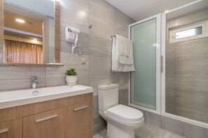 A modern bathroom with a wooden vanity, a white toilet, a glass shower enclosure, and a mirror above the sink. - Zante Sky Suites (Zakynthos)