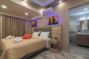 A modern hotel room with a large bed, a nightstand, an air conditioning unit, and a bathroom with a mirror and towel rack. - Zante Sky Suites (Zakynthos)