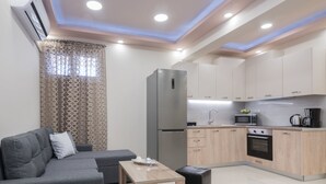 A modern kitchen with a refrigerator, microwave, oven, and sink. There is a grey sofa and a small table with a tray. - Zante Sky Suites (Zakynthos)