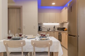 A modern kitchen with a dining table set for two, equipped with a refrigerator, microwave, and coffee maker. - Zante Sky Suites (Zakynthos)