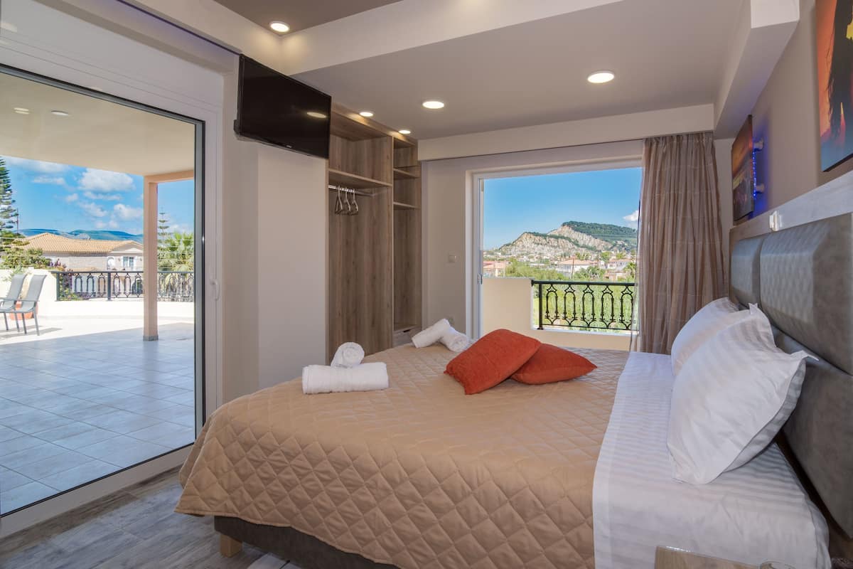 A bedroom with a large bed, a balcony with a view, and a sliding door to an outdoor area.