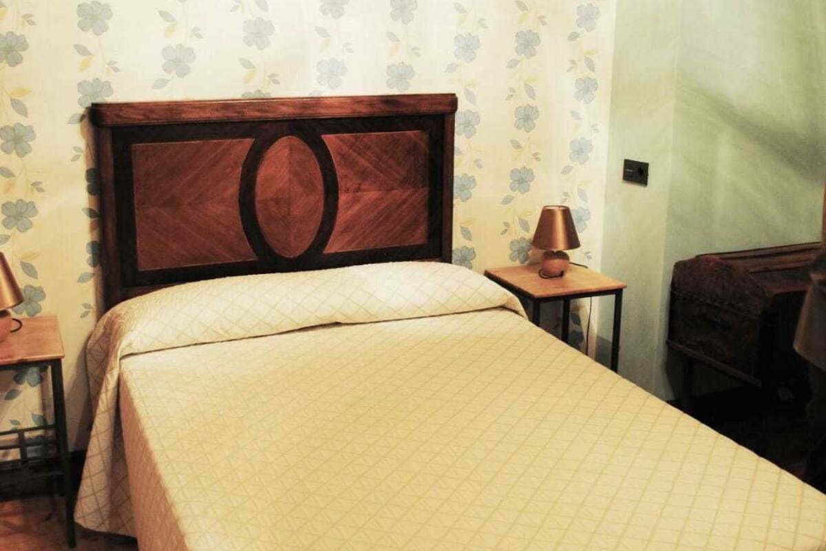 Una cama individual con cabecera de madera, una mesita de noche con lámpara y papel tapiz floral.