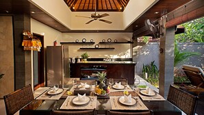 Un comedor moderno con una mesa de vidrio, sillas de mimbre y un ventilador de techo.