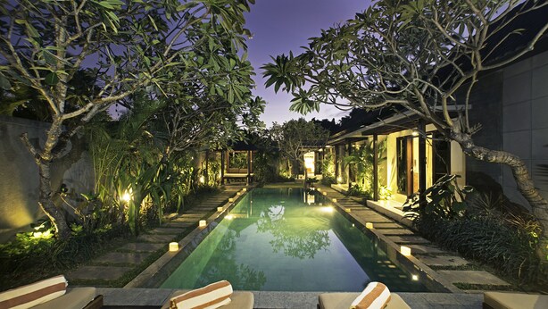Un área de piscina exterior tranquila con sillones reclinables y un sendero bien iluminado.
