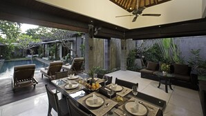 Un amplio espacio exterior con comedor, piscina, asientos y ventilador de techo.