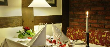 A table set for two with a candle, glasses, and a vase of flowers.