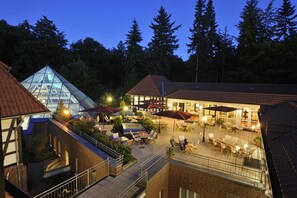 A courtyard with outdoor seating, a glass structure, and a building with a red roof. - Vila Vita Burghotel Dinklage (Dinklage)