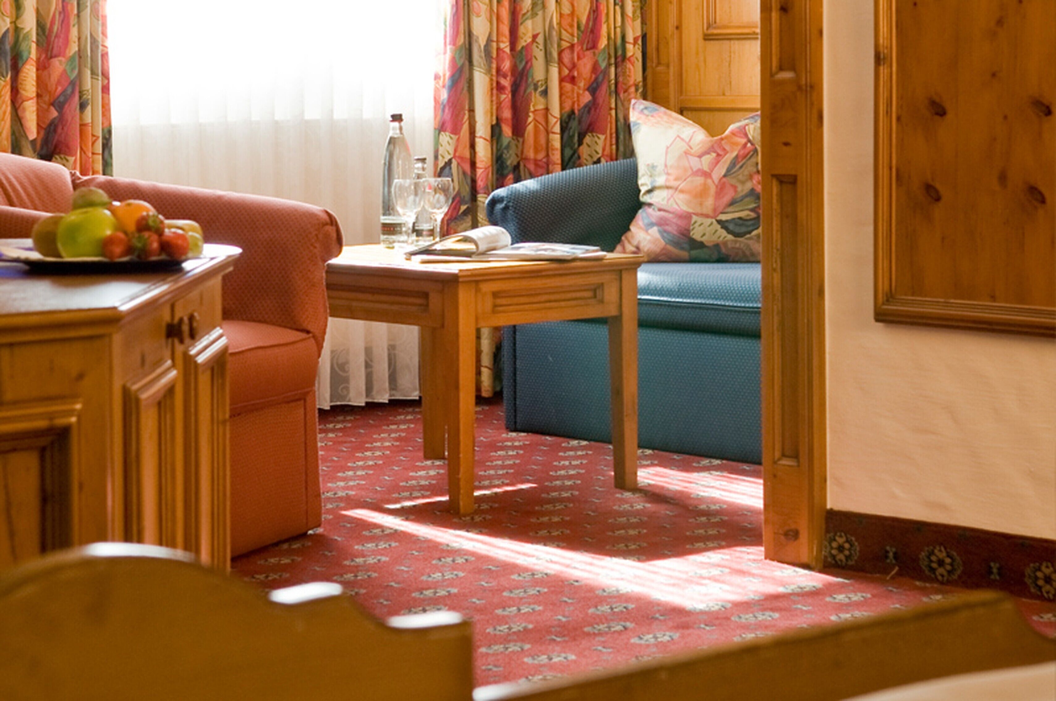 Ein gemütliches Wohnzimmer mit einem Holztisch, einem blauen Sofa und einem roten Teppich mit Muster.