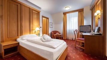 A hotel room with a bed, a desk with a computer, a chair, a television, and a lamp.