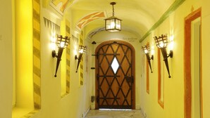 Un couloir avec une porte en bois, des appliques murales décoratives et un sol carrelé.