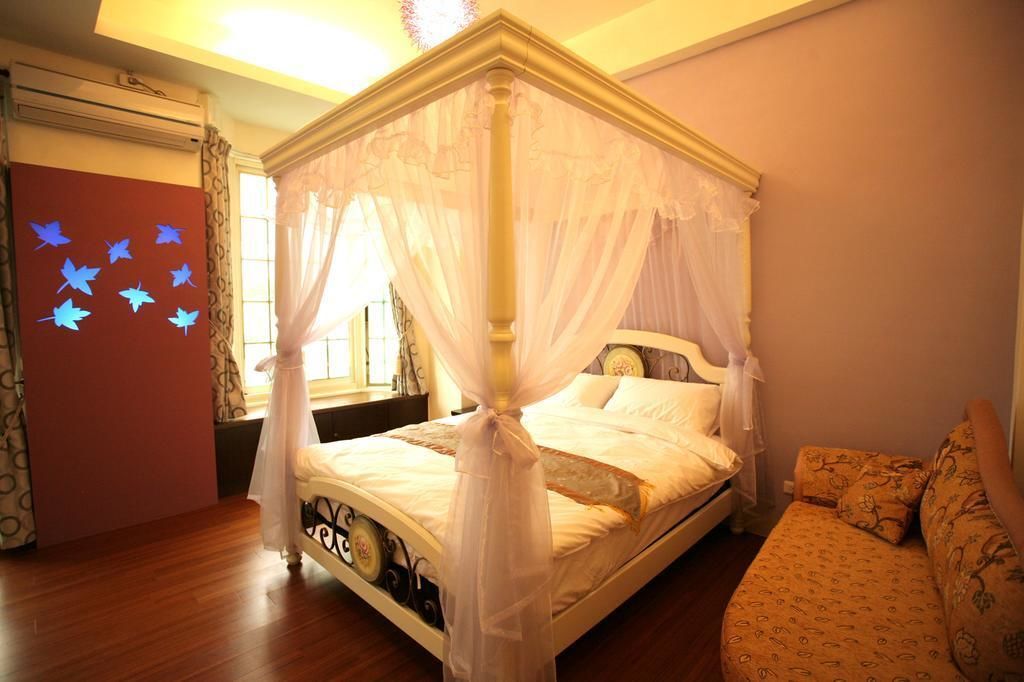 Un letto a baldacchino con tenda bianca, pavimento in legno, un divano decorato con motivi e una parete con adesivi a forma di farfalla.