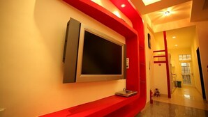 Un interior moderno con un televisor de pantalla plana grande montado en una pared roja decorativa, un pasillo que conduce a una puerta y una pequeña mesa con un control remoto.