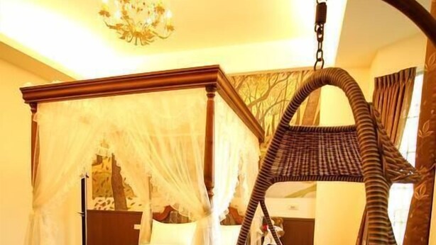 Una cama con dosel y cortinas, un sillón colgante de mimbre y un candelabro.